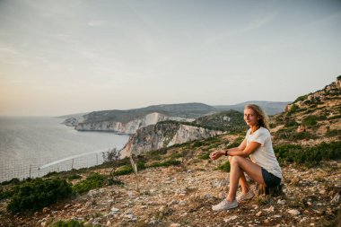 Kadın turist rahatlıyor ve denizde kayaları seyrediyor.