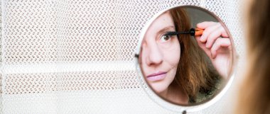 Aynadaki kadın makyaj yapıyor.