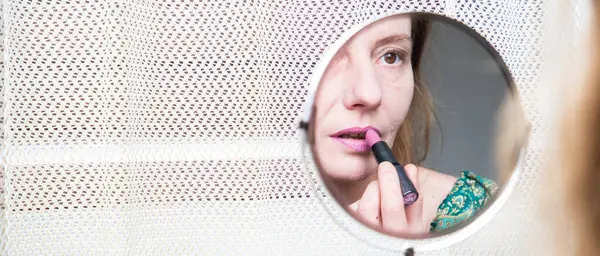 woman in mirror applying makeup