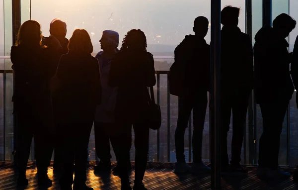 silhouettes of people watching sunset over city