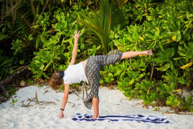 Kadın tropikal plajda yoga yapıyor.