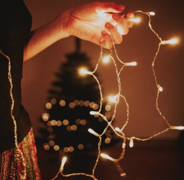 Ağacı süsleyen bir kadının elinde noel ışıkları