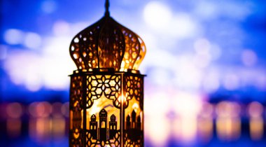 Gece yanan mum ve arka planda cami ile süslenmiş Arapça bir fener. Müslüman kutsal ayı Ramazan Kareem için kutlama kartı.