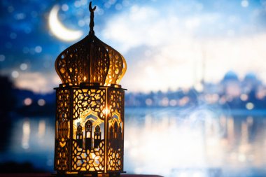 Gece yanan mum ve arka planda cami ile süslenmiş Arapça bir fener. Müslüman kutsal ayı Ramazan Kareem için kutlama kartı.