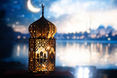 Gece yanan mum ve arka planda cami ile süslenmiş Arapça bir fener. Müslüman kutsal ayı Ramazan Kareem için kutlama kartı.