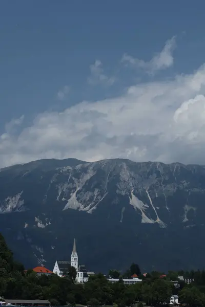 Yüksek kulesi olan beyaz bir kilise, yüksek kayalık dağlar ve mavi gökyüzü tarafından çerçevelenmiştir..