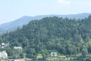 Ormanla kaplı bir tepenin eteklerine kurulmuş binalar, berrak, mavi bir göl..