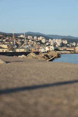 Rıhtımın önü bulanık. Altın saat boyunca arka planda vinçler ve konut binaları görünüyor..