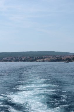 Kıyı kasabası ve tepeleriyle, derin mavi denizi aşan bir teknenin bıraktığı parlak beyaz bir iz..