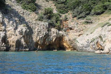 Hırvat sahili boyunca uzanan altın renkli kayalıklar arasında gölgeli bir deniz mağarası açılıyor.