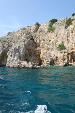 Keskin kaya dokuları ve pas rengi mineral çizgileri turkuaz kıyı sularıyla buluşur..