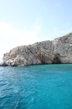 Açık mavi gökyüzünün altında turkuaz denizden yükselen dramatik uçurumları olan kayalık bir sahil. Huzurlu ve uzak bir deniz manzarası bir tekneden alındı..