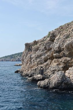 Açık mavi gökyüzünün altında turkuaz denizden yükselen dramatik uçurumları olan kayalık bir sahil. Huzurlu ve uzak bir deniz manzarası bir tekneden alındı..