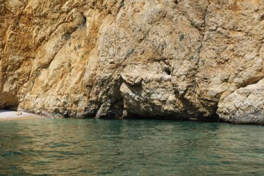 Açık mavi gökyüzünün altında turkuaz denizden yükselen dramatik uçurumları olan kayalık bir sahil. Huzurlu ve uzak bir deniz manzarası bir tekneden alındı..