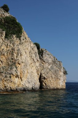 Engebeli bir kireçtaşı kayalığı berrak mavi suyun üzerinde yükseliyor. Parlak, güneşli bir günde yakalanan bu uzak kıyı manzarasının dokuları ve gölgeleri doğal güzelliğini arttırır..