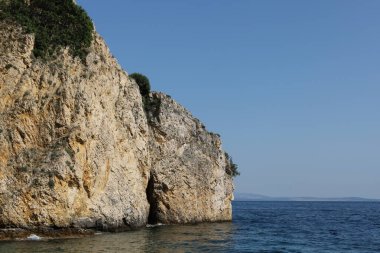 Engebeli bir kireçtaşı kayalığı berrak mavi suyun üzerinde yükseliyor. Parlak, güneşli bir günde yakalanan bu uzak kıyı manzarasının dokuları ve gölgeleri doğal güzelliğini arttırır..