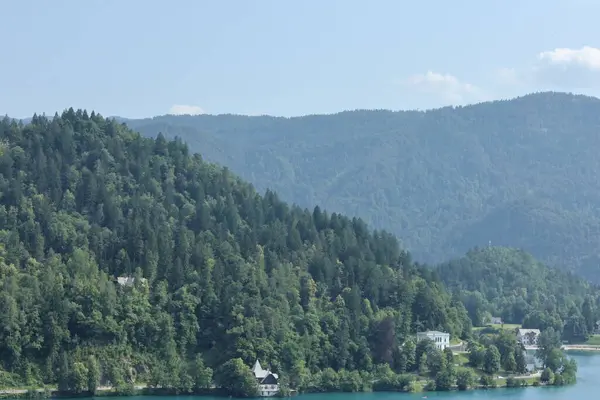 Berrak yeşil tepelerle çevrili huzurlu göl ve berrak bir yaz gökyüzü altında küçük evler..