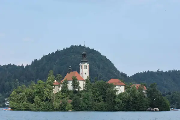 Bled Island 'daki ikonik kilise gölün üzerinde yeşil tepeler ve mavi gökyüzü üzerine kurulmuş..