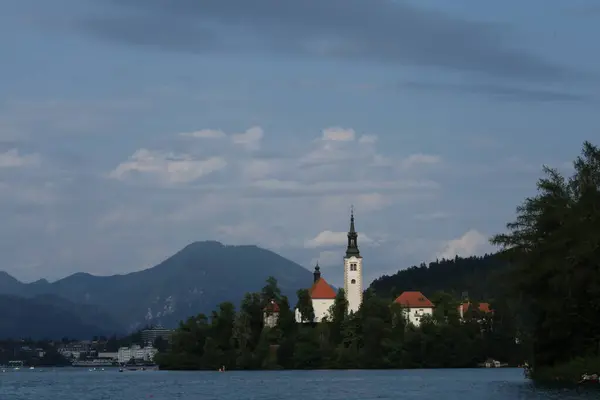 Bled Island 'ın kasvetli manzarası bulutlu bir gökyüzünün altında, göl ve dağ siluetleri ile.