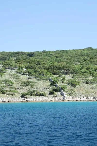Terk edilmiş eski bir taş ev yemyeşil bitki örtüsüyle çevrili kayalık bir sahil şeridinde duruyor. Yapı yıpranmış ve tarihsel görünüyor, insan yapımı mimariyle dokunulmamış doğa arasında bir tezat oluşturuyor..