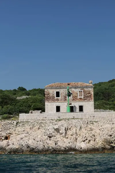 Engebeli kayalık bir kıyı denizin sakin mavi sularıyla buluşur ve yoğun yeşil bitki örtüsü tepeye tırmanır. Kaya dokusu ve gür yeşillik arasındaki zıtlık zengin bir doğal manzara yaratır..