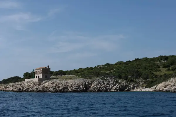 Hırvatistan 'ın yemyeşil tepeleri ve kayalık kıyılarıyla çevrili eski bir deniz fenerinin uzak manzarası.