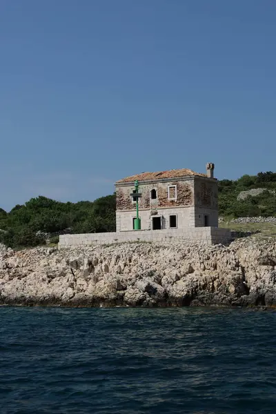 Terk edilmiş bir deniz feneri açık mavi gökyüzünün altındaki kayalık bir Hırvat kıyı şeridinde bulunuyor.