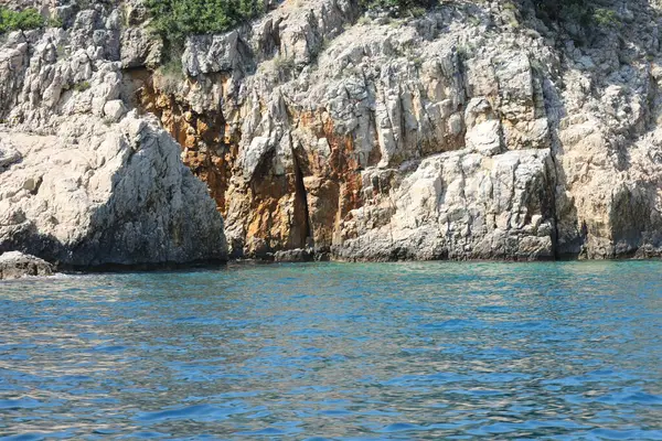 Turkuaz denizin üzerinde kırmızı ve beyaz desenli renkli kıyı kaya oluşumları.