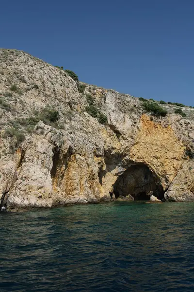 Güneşli turuncu ve sarı kayalık uçurumlarda zümrüt sularının üzerinde bir mağara girişi..