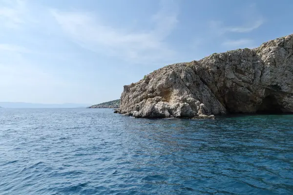Açık mavi gökyüzünün altında turkuaz denizden yükselen dramatik uçurumları olan kayalık bir sahil. Huzurlu ve uzak bir deniz manzarası bir tekneden alındı..