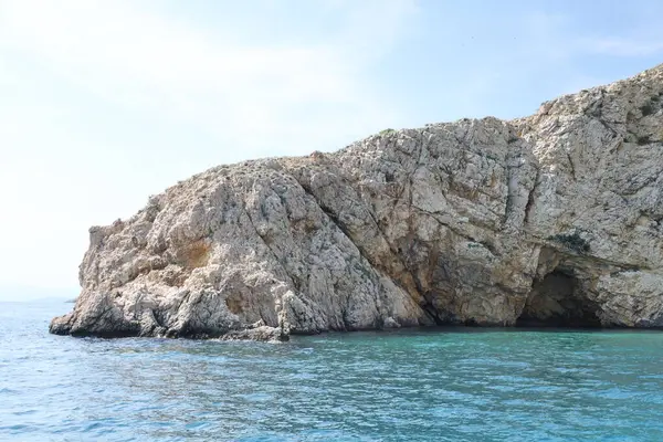 Açık mavi gökyüzünün altında turkuaz denizden yükselen dramatik uçurumları olan kayalık bir sahil. Huzurlu ve uzak bir deniz manzarası bir tekneden alındı..