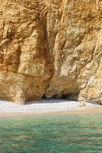 Engebeli bir kireçtaşı kayalığı berrak mavi suyun üzerinde yükseliyor. Parlak, güneşli bir günde yakalanan bu uzak kıyı manzarasının dokuları ve gölgeleri doğal güzelliğini arttırır..