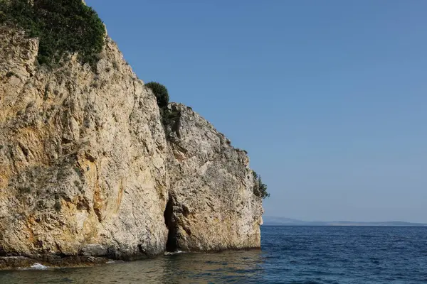 Engebeli bir kireçtaşı kayalığı berrak mavi suyun üzerinde yükseliyor. Parlak, güneşli bir günde yakalanan bu uzak kıyı manzarasının dokuları ve gölgeleri doğal güzelliğini arttırır..