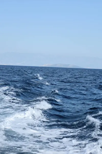 Tepeler ve açık gökyüzü tarafından çerçevelenmiş canlı mavi sularda bir kayığın uyanması çarpıcı bir şekilde kıvrılır..