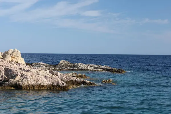 Yıpranmış kaya yüzeyinin yakın çekimi, parlak bir gökyüzünün altında denizle buluşuyor, jeolojik dokusu ve kıyı karakteri zengin..