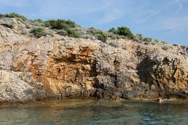 Su kenarındaki kayalık kayalıkların detaylı görüntüsü, arka planda canlı taş katmanları ve okyanus mavilerini gösteriyor.