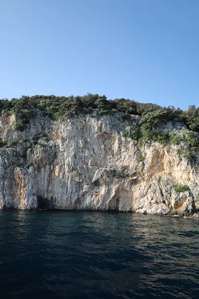 Parlak yeşil çalılar denizin üzerindeki engebeli uçurum kenarını kaplıyor. Taş yüzeyinde zengin renkler ve desenler var..