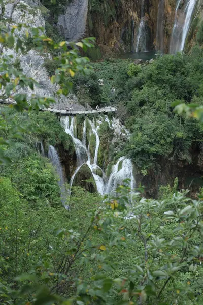 Hırvatistan 'da dinamik bir doğal manzara sunan, turistlerle dolu ahşap bir geçidin altındaki kayalara düşen şelaleler görülüyor..