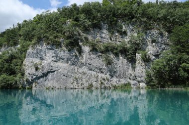 Dik kayalıklar parlak güneşli bir günde aşağıdaki el değmemiş mavi göl suyuna yansıyor..
