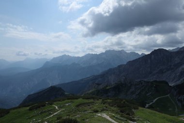 Alpler 'in puslu ve kasvetli manzarası dağların katmanlarıyla ağır bulutlarla dolu bir gökyüzünün altındaki mesafeye doğru kayboluyor..