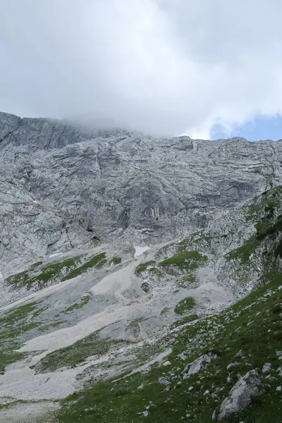Gri taş, yeşil yamaçlar ve dağınık kar parçalarıyla gizlenmiş bir dağdan çarpıcı bir manzara..