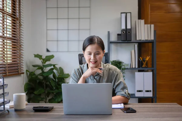 Beautiful asian businesswoman, entrepreneur, or freelance in casual clothes sitting at desk with paperworks and laptop casually working online in living room at home. At home, business concept.