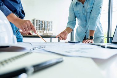 Genç bir mühendis ya da mimar, kıdemli ya da patronuyla konuşuyor, inşaat projesi planının grafik tasarımını çiziyor ve planlar ve diğer ekipmanlarla birlikte çalışma masasında gelişim için tartışıyorlar. Mühendislik ve Takım