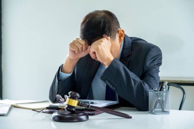 Bir avukat ya da avukat önemli dosya ve belgelerle çalışma masasında oturuyor, mahkemeye çıkarılmadan önce müvekkili için davayı çözmeye çalıştıktan sonra stresli ve baskı altında hissediyor..