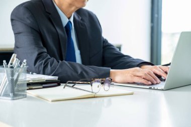 Resmi kıyafetli avukat ya da avukat, elinde kağıt dosyaları ve önemli belgelerle masada oturuyor ve mahkemeye getirilecek davaların önemli bilgilerini görmek için dizüstü bilgisayarla çalışıyor. Hukuk, adalet kavramı.