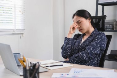 Stresli bir iş kadını olan şirket çalışanı, iş yerinde dizüstü bilgisayar ve kağıt işleriyle masasında oturuyor, düşünüyor, düşünüyor ve iş konuları, planlar, yatırım sonuçları ve riskleri hakkında endişe ediyor. İş konsepti.