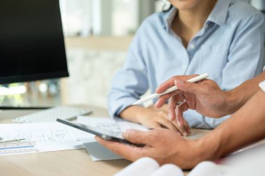 İki kadın ve erkek mühendis, müteahhit veya mimar birlikte çalışıyor, tablet ekranı işaret ediyor, inşaat projesinin grafik tasarımını çiziyor ve birçok ekipmanla birlikte çalışma masasında gelişim için tartışıyorlar. Mühendislik ve Takım Çalışması konsepti.