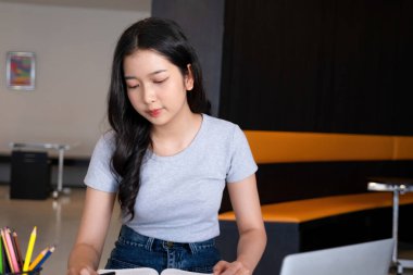 Genç bir kadın ya da iş kadını modern bir çalışma alanında özenle oturuyor, güvenilir laptopuyla çalışmaya dalmış ve yararlı bilgilerle zihnini zenginleştirmek için kitap okumaya kendini adamış..