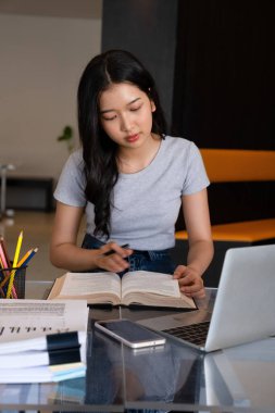 Genç bir kadın ya da iş kadını modern bir çalışma alanında özenle oturuyor, güvenilir laptopuyla çalışmaya dalmış ve yararlı bilgilerle zihnini zenginleştirmek için kitap okumaya kendini adamış..