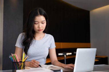 Genç bir kadın ya da iş kadını modern bir çalışma alanında özenle oturuyor, güvenilir laptopuyla çalışmaya dalmış ve yararlı bilgilerle zihnini zenginleştirmek için kitap okumaya kendini adamış..